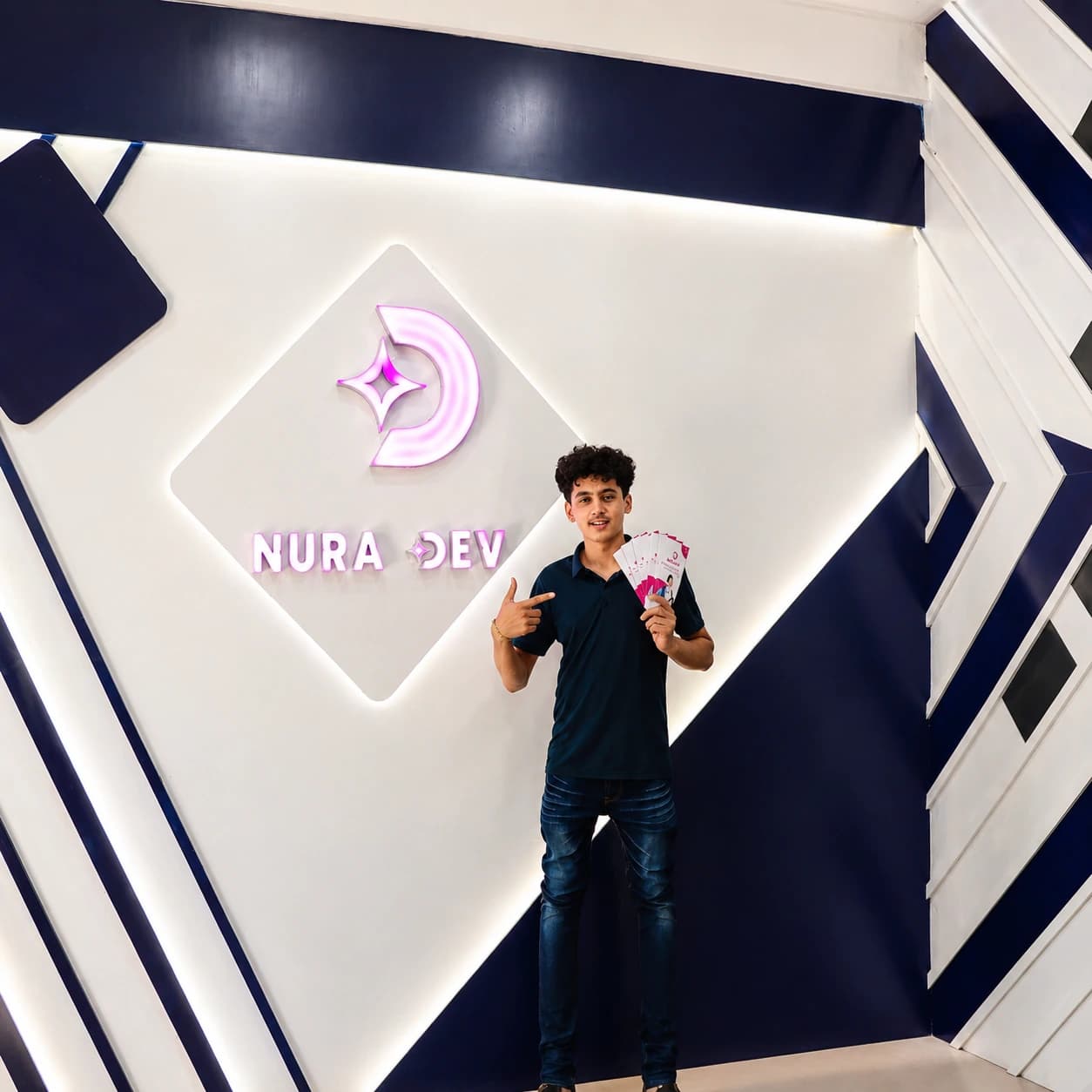 Nura Dev student holding course brochures beside the campus logo