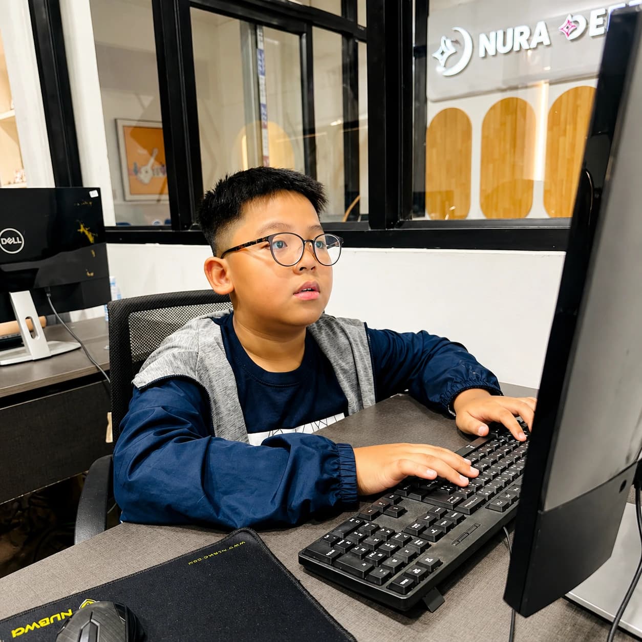 Nura Dev learner using a desktop computer under the campus logo